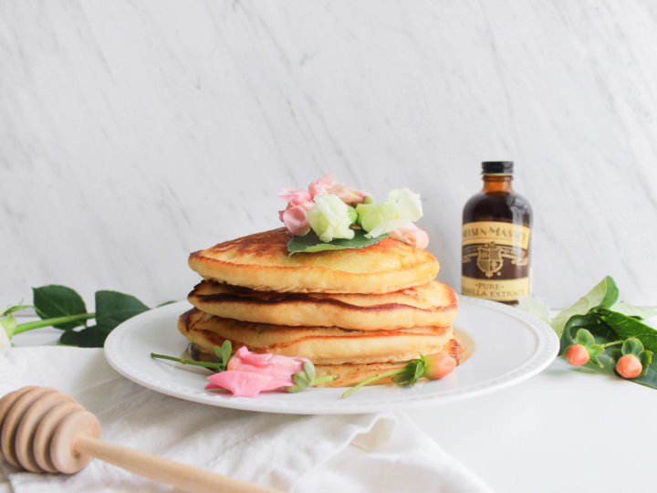 stack of pancakes with honey brush and bottle of Nielsen-Massey vanilla