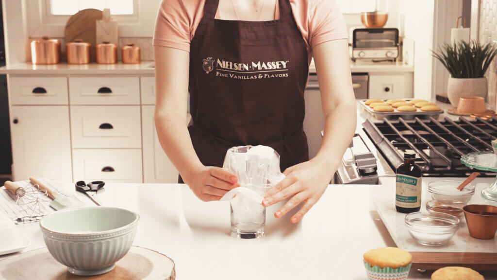 Woman placing pastry bag in tall cup to stabilize it while she fills with frosting