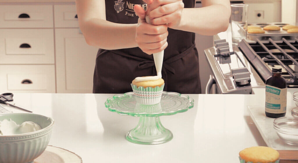 Woman piping frosting onto cupcake