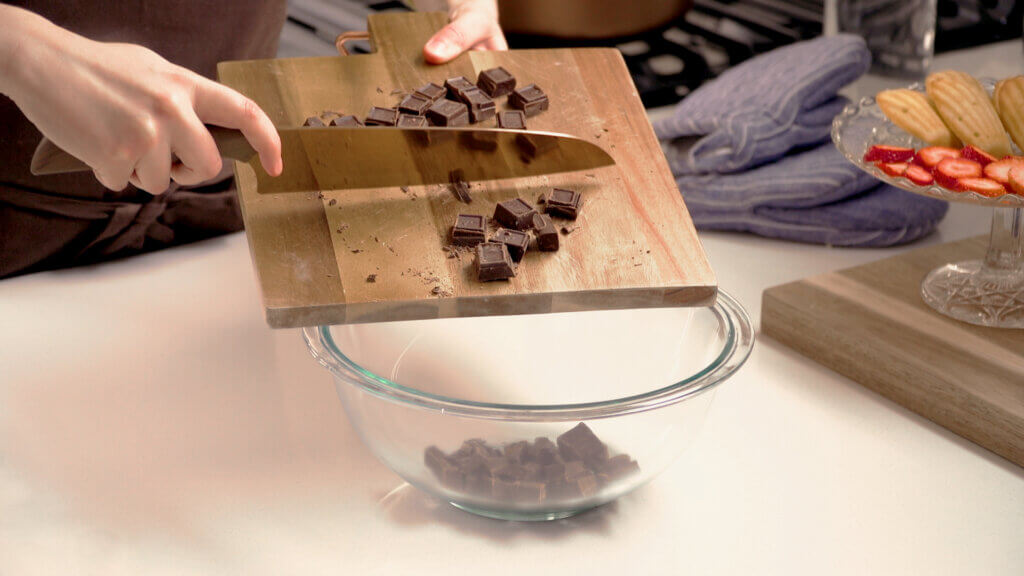 Wood cutting board with pieces of chopped chocolate going into a bowl
