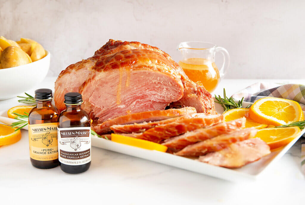 slices of glazed slow-cooked ham on a platter with vanilla and orange extract bottles